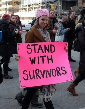 Stand with survivors Photo of a woman with a placard: Stand with survivors