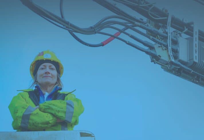 Photo of a woman in industrial work gear and yellow hard hat with their arms crossed.