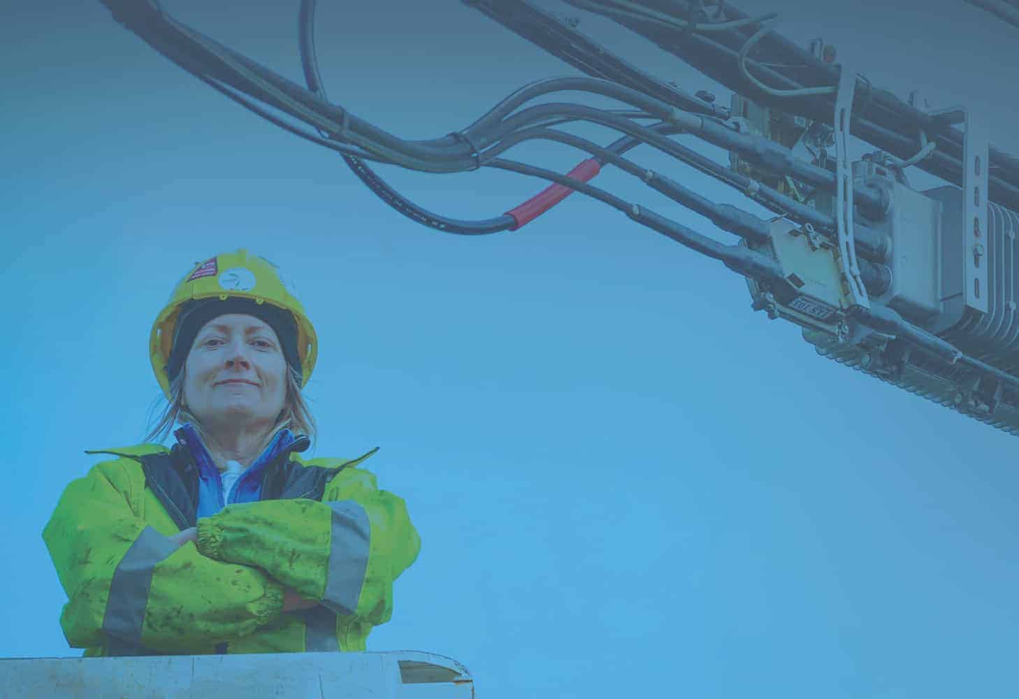 Photo of a woman in industrial work gear and yellow hard hat with their arms crossed.