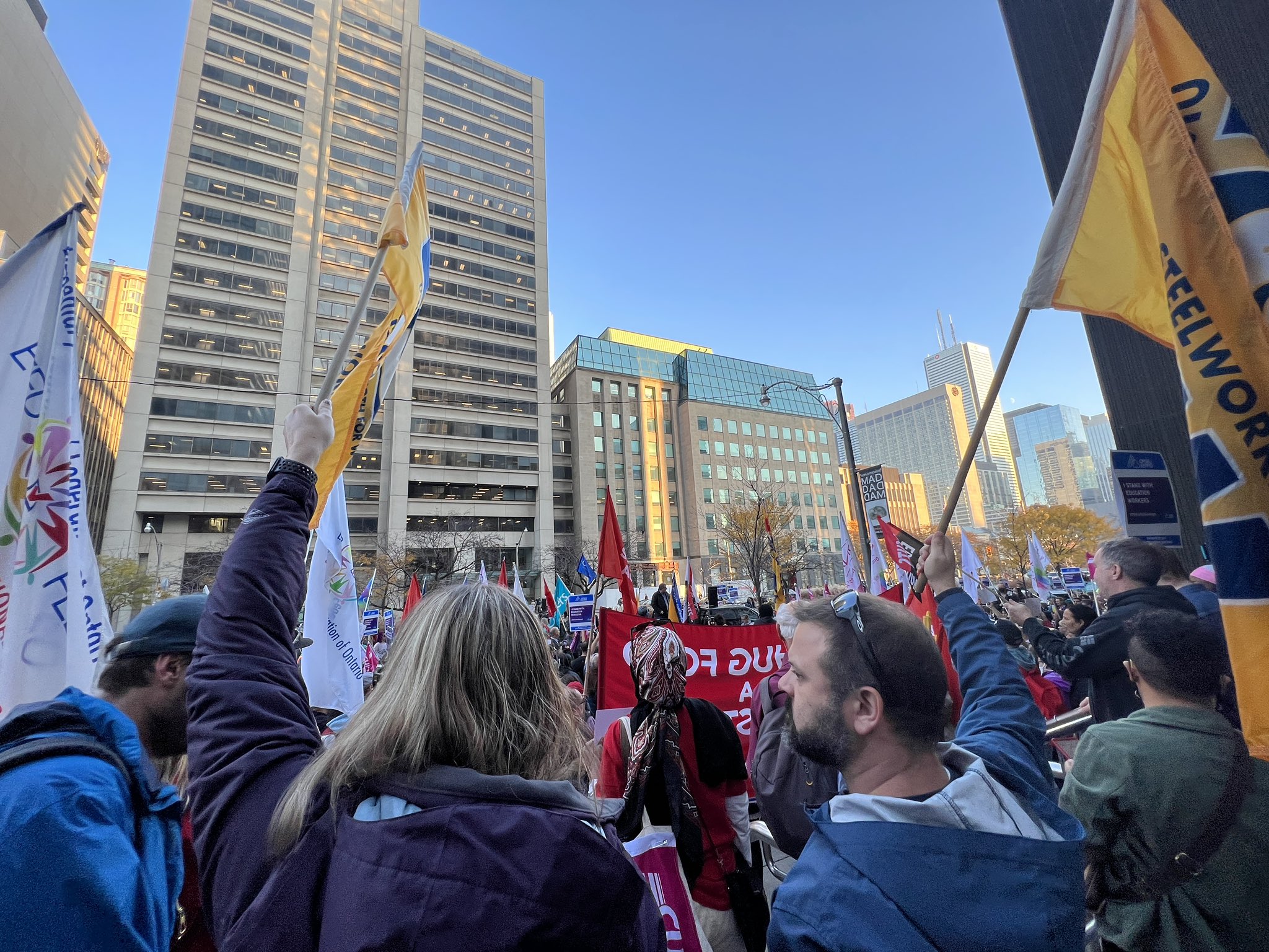 Image: people gather outdoors downtown with flags to show support for education workers