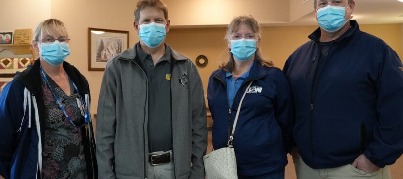 Four people wearing masks, standing side by side, indoors