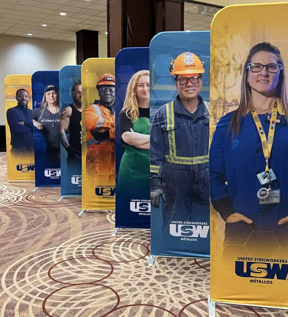 Image: a line-up of seven stand-up banners picturing members of the steelworkers union