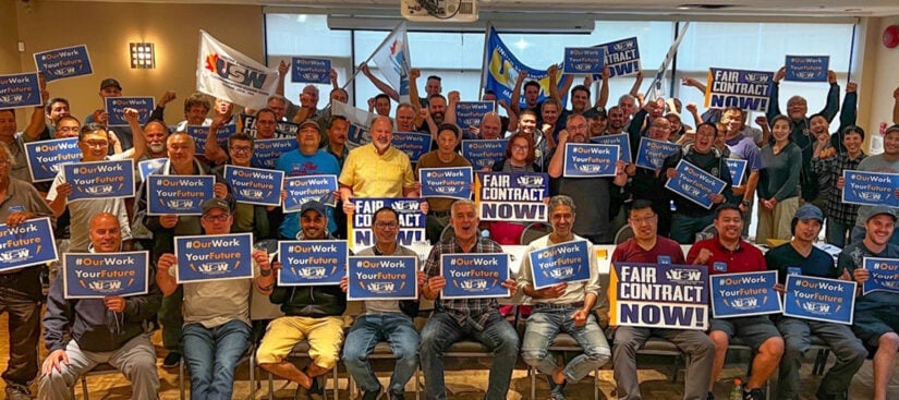 A bunch of members from Rogers sitting and standing together holding signs to support bargaining