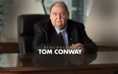 A man sitting behind a desk with a text saying Remembering Tom Conway.