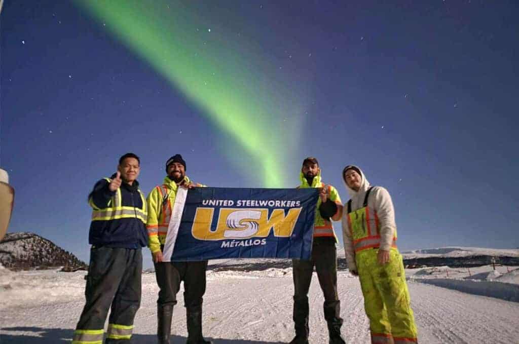 Workings from Parsons Inc holding a USW flag under the Northern Lights