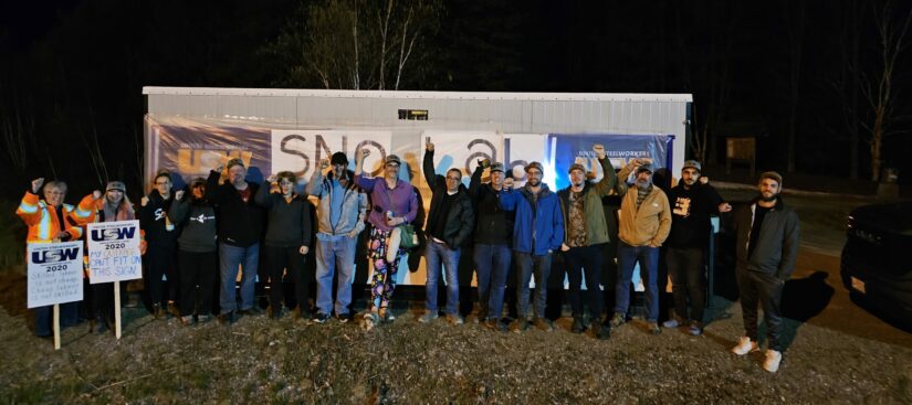 A group of people standing side-by-side outdoors, in front of a trailer. The photo was taken in the evening, marking the beginning of a strike, so the surroundings are dark.
