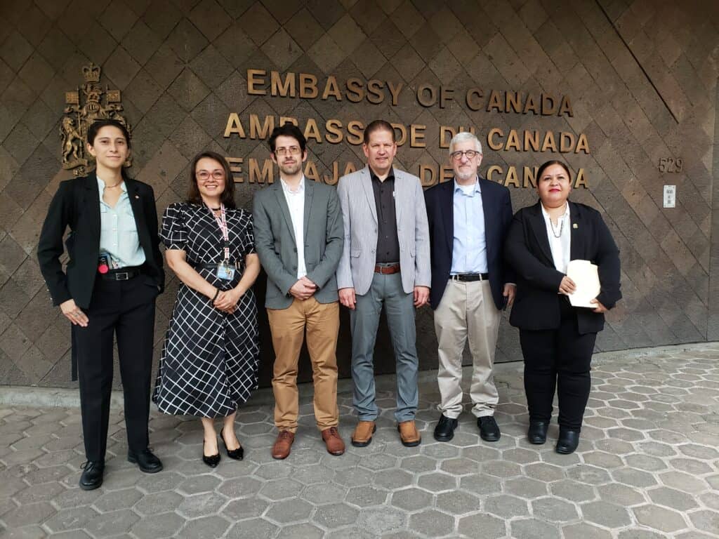 A photo of 6 people standing side by side in front of a the Embassy of Canada building in Mexico City.