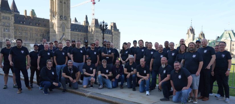A group of people wearing blue shirts and taking a photo outdoor. The Canadian Parliament Building appears in the background.
