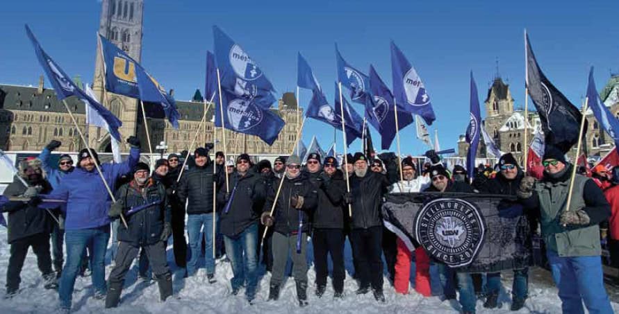 Picture: A group of people taking a photo during a rally outside of the Parliament Hill. They are wearing winter clothes and standing on the snow. Some of them are raising blue flags with the Métallos and USW logos. The Canadian Parliament building is visible in the background.