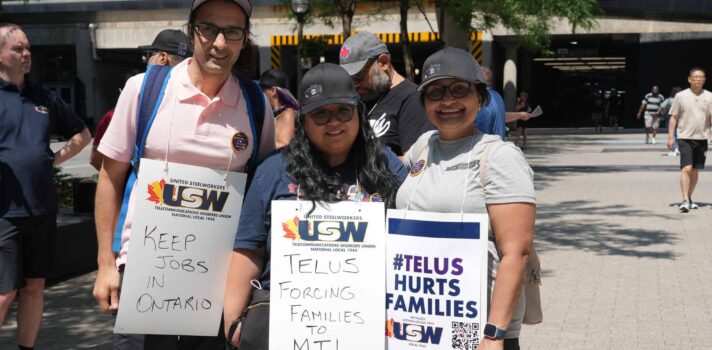 Image: three people are facing the camera, outdoors on a sunny day. They are wearing placards reading 