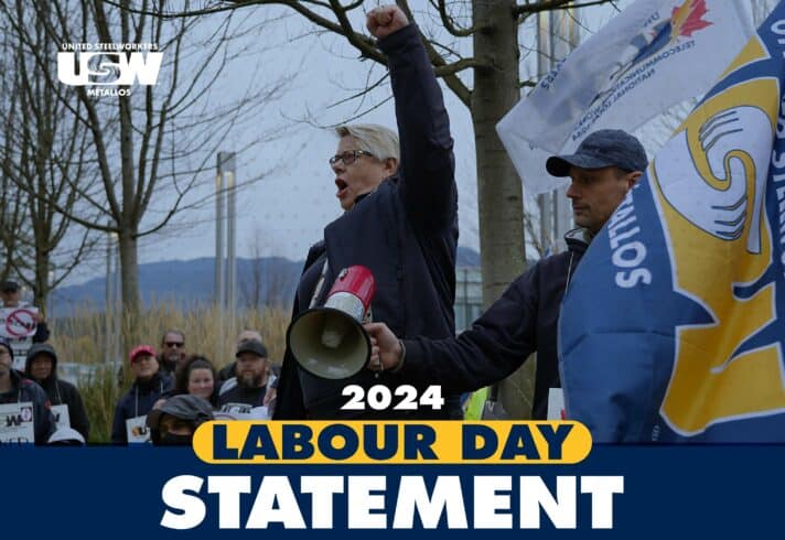 A person pumping its fist during a picket line. People holding signs appear in the background of the photo. There text saying: 2024 Labour Day Statement.