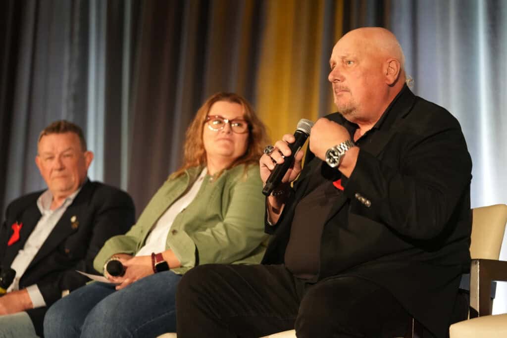 Three people sitting on the stage during the panel one of them is holding the microphone