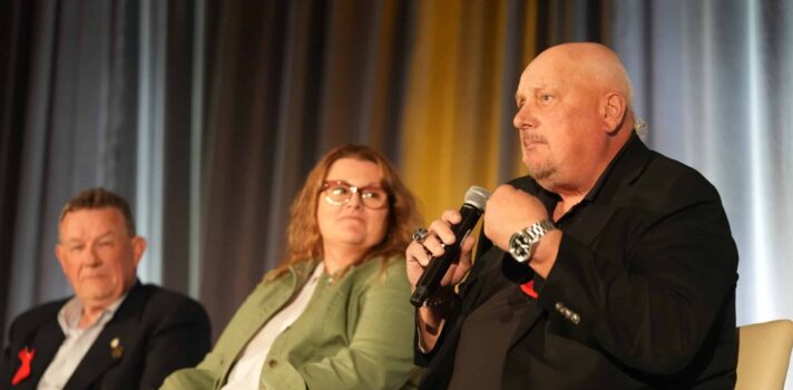 Three people sitting on the stage during the panel one of them is holding the microphone