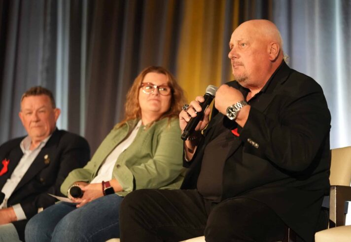 Three people sitting on the stage during the panel one of them is holding the microphone