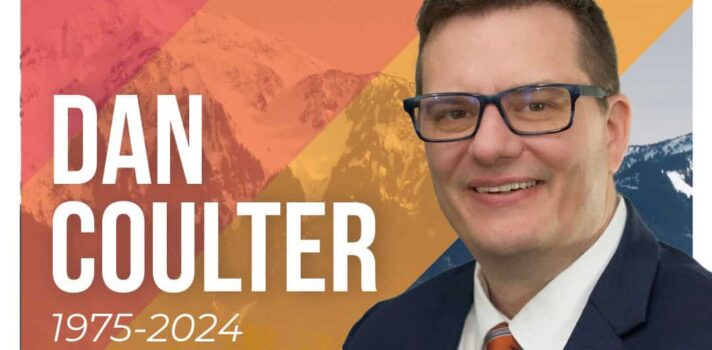 Man in suit with tie. Orange stripes in background with mountain scenery with the BC NDP logo