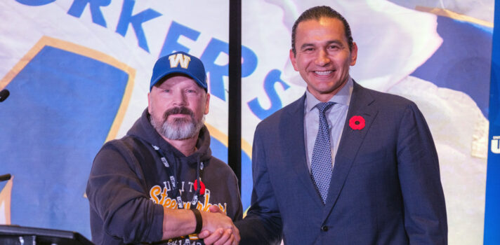 Mike Pulak shaking hands with Premier Wab Kinew in front of USW flag background