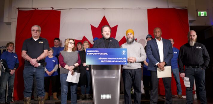 Director of the United Steelworkers union Marty Warren stands behind a podium next to Jagmeet Singh, Leader of the federal NDP, and Kevon Stewart, USW District 6 Director, and among other labour leaders.