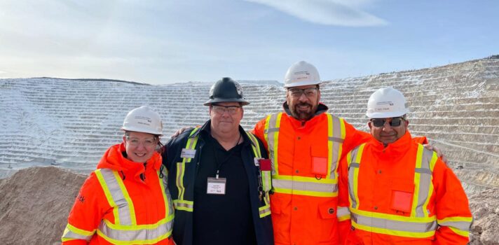 Four people in safety gear and hard hats smiling. 