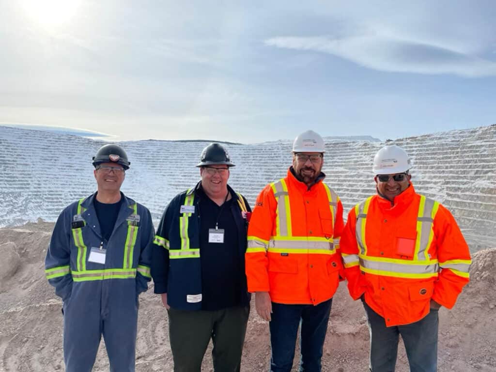 Four people in safety gear and hard hats smiling.