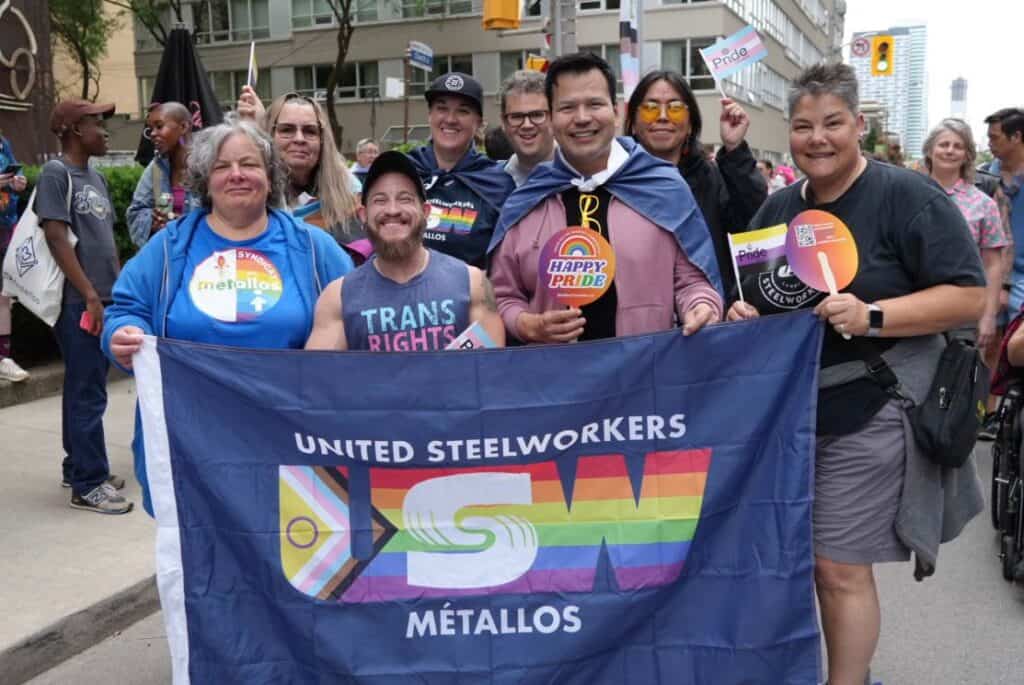 four people standing beside each other holding bleu flag with the Rainbow community logo