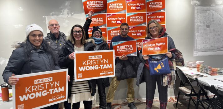 A group of people in a campaign office holding orange campaign signs.