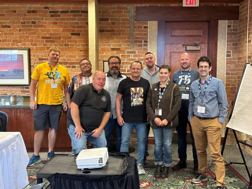A group of people standing in front of a table indoor, posing to the camera during a workshop.