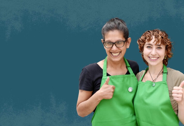 Two people wearing green Starbucks aprons smiling and showing thumbs up