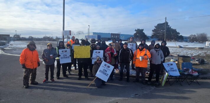 A group of people standing and holding signs in front of a building at a parking lot.