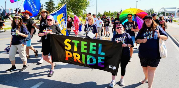 A group of people marching in the Calgary Pride Parade holding a banner that reads Steel Pride.